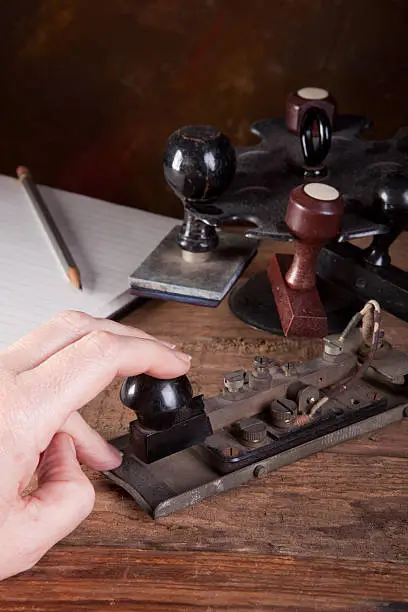 Hand tapping morse code on an antique telegraph machine