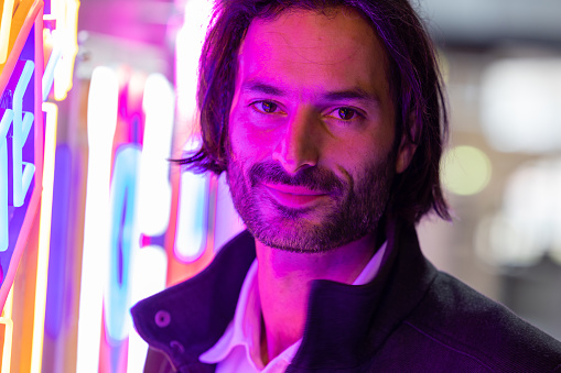 portrait of a smiling young man with long hair lit by a neon sign