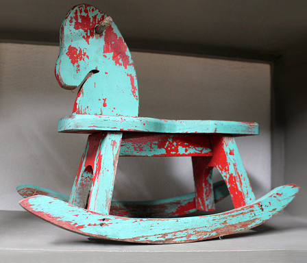 Wooden Rocking Horse with red and turquoise peeling paint - on a shelf at the antique stores