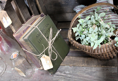 Antique books tied with twine with a price tag for sale at the antique stores - leaning against an old wooden crate with an old milk bottle and a plant in a basket