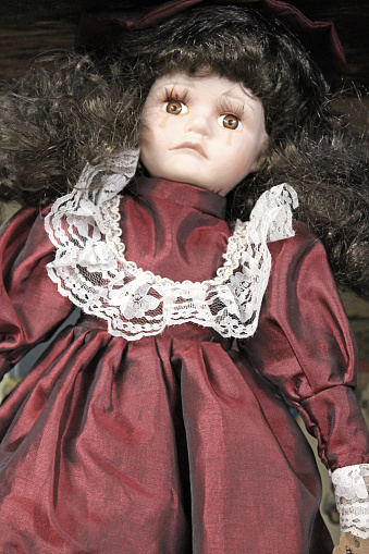 A creepy looking porcelain doll with brown hair, a burgundy dress with white lace at the antique stores