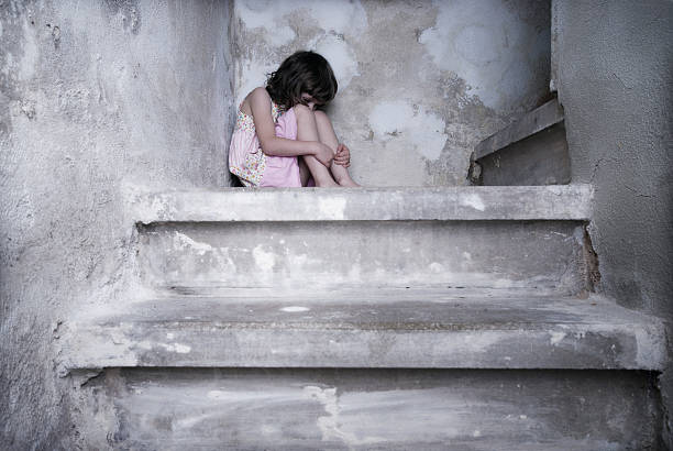 A young girl in pink cowering at the top of the stairs little girl sits lonely on cold stairs sad girl crouching stock pictures, royalty-free photos & images