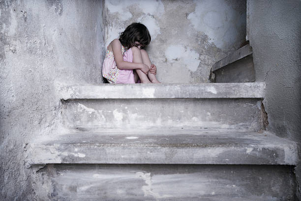 A young girl in pink cowering at the top of the stairs stock photo