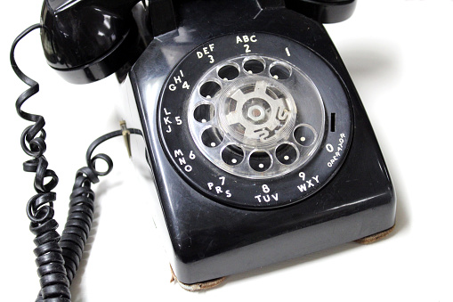 Retro Black rotary dial phone with coiled up cord at the antique stores - white background