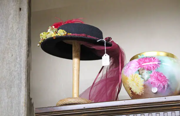 A painted antique vase and hat on hatstand on a shelf at the antique stores