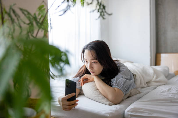 istock Young woman using smartphone on bed in the morning - lying on front 1473071740