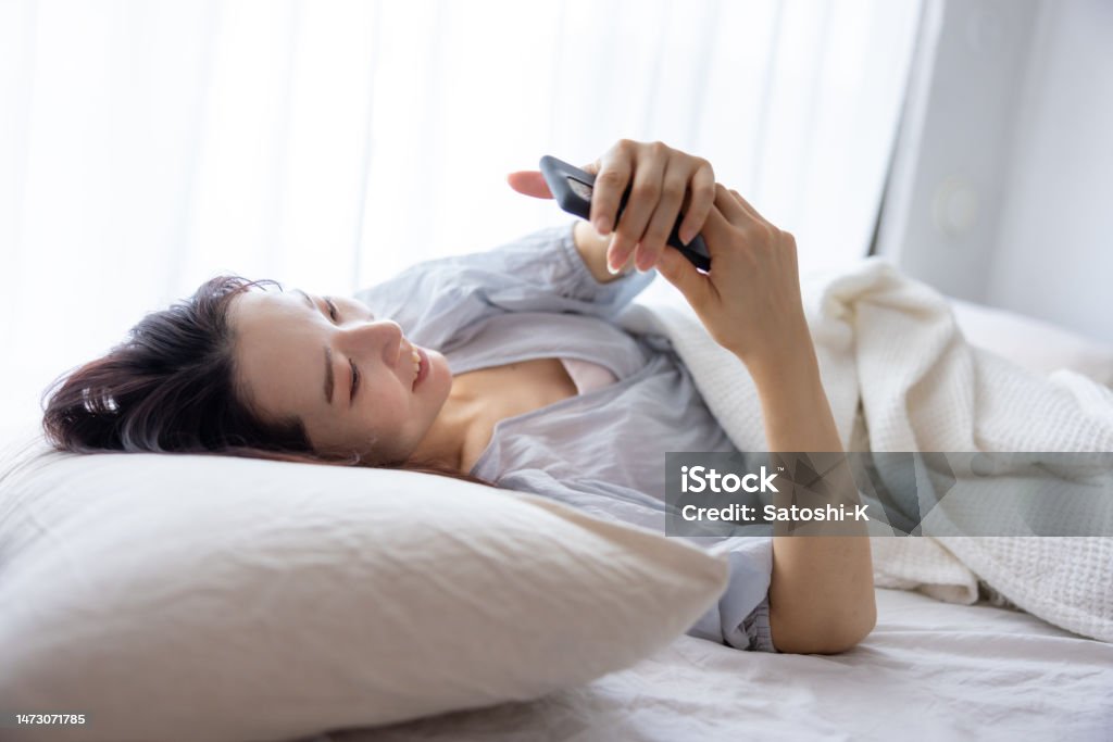 Young woman using smartphone on bed in the morning - smiling Pillow Stock Photo