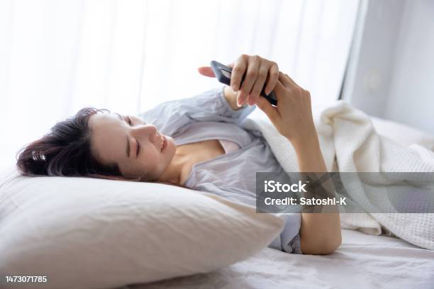 Young Woman Using Smartphone On Bed In The Morning Smiling Stock Photo - Download Image Now