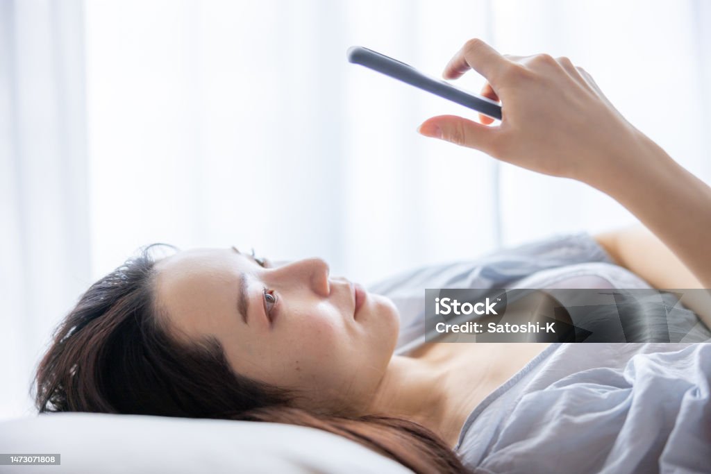 Close-up of young woman using smartphone on bed in the morning Adult Stock Photo