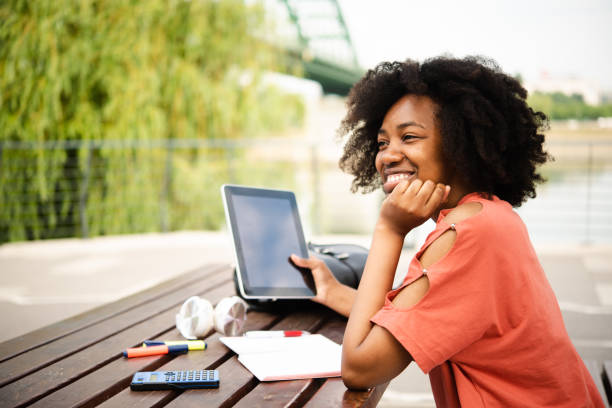 African American young woman making a business plan outdoors Beautiful African American young woman sitting outdoors and working online on her digital tablet ipad calculator stock pictures, royalty-free photos & images