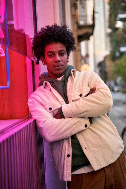 selbstbewusster, cooler junger afroamerikaner, der im neonlicht auf der straße steht. - afro amerikanischer herkunft stock-fotos und bilder