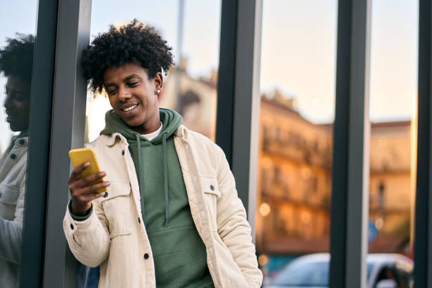 cooler afroamerikaner, der ein mobiltelefon benutzt, steht im glasgebäude der stadt. - afro amerikanischer herkunft stock-fotos und bilder