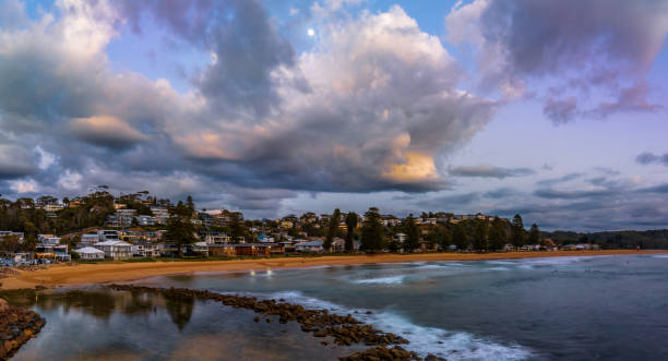 istock Sunrise shorescape with houses, clouds and the moon 1473076245