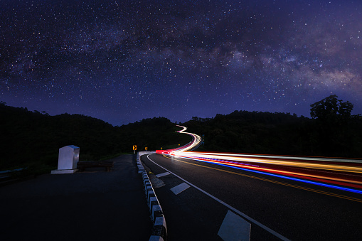 Photograph long exposure shot  car light at night scene blue sky and galaxy or star milky way background, at Curved Road No.3 or Route No.1081 over top of mountains in Santisuk - Bo Kluea District, Nan province, Thailand. Popular places for tourists.
