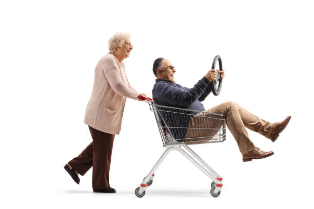 starsza kobieta pcha dojrzałego mężczyznę do wózka sklepowego trzymającego kierownicę - sale zdjęcia i obrazy z banku zdjęć