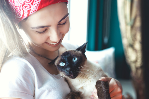 young woman hugging her cat in front of the window