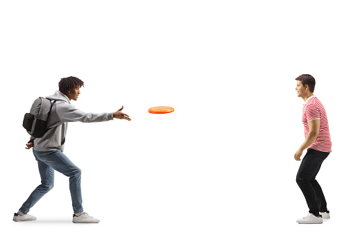 Full length profile shot of a young african american man throwing a flying disc with a young caucasian man isolated on white background