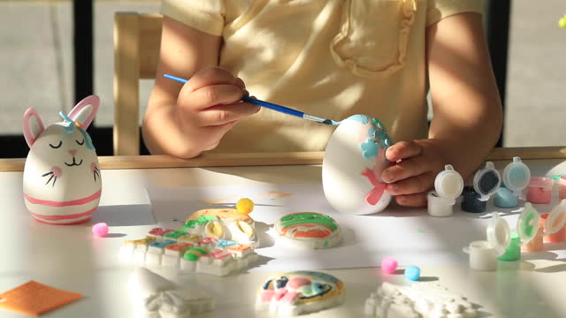 A small child decorates an Easter egg. Ideas of Easter crafts with children.