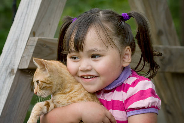 Cute little brunette girl in pigtails holding her orange kitten