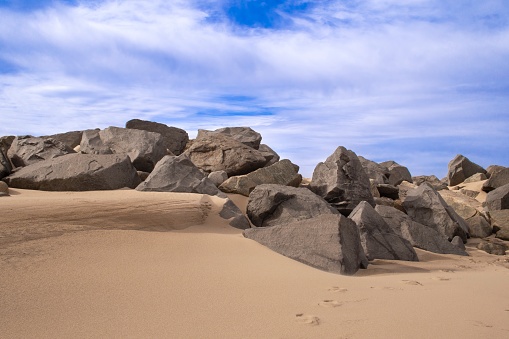 Sandy beach with boulders, large rocks. Blue sky with wispy clouds on a winter's day, Sandy Hook Beach, New Jersey, USA, part of Gateway National Recreation Area, popular for ocean swimming, bird watching, camping, boating and hiking.
