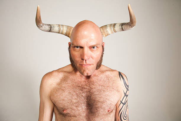 Shirtless Man With Horns A shirtless man, tattoo on his arm, stands looking directly into the camera. Behind him, horns are held up, making it appear as though they grew right out of his head. feirce stock pictures, royalty-free photos & images