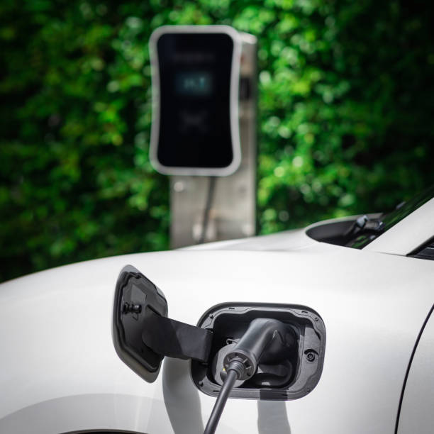 istock Side view progressive EV car with charging station, green foliage background. 1473096739