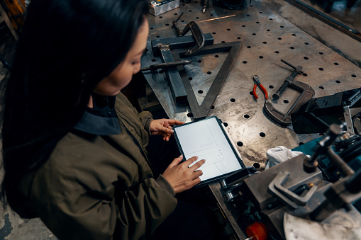 Mid adult female using a digital tablet in a metal fabrication workshop in Japan