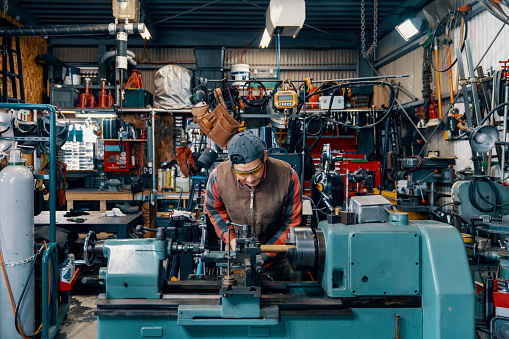 Medium shot of a mid adult man working on a lathe in a metal fabrication workshop