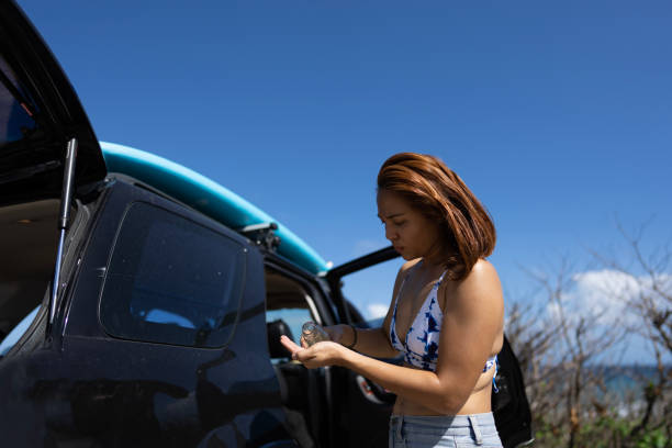 mulher chinesa asiática que aplica óleo de coco no cabelo antes de surfar no estacionamento ao lado do suv - beach parking lot car equipment - fotografias e filmes do acervo