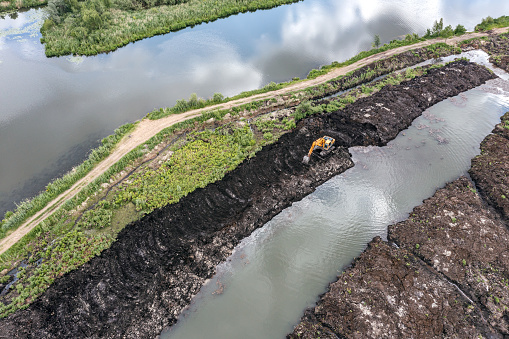 excavator digging drainage ditch in peat extraction site. aerial view with drone.