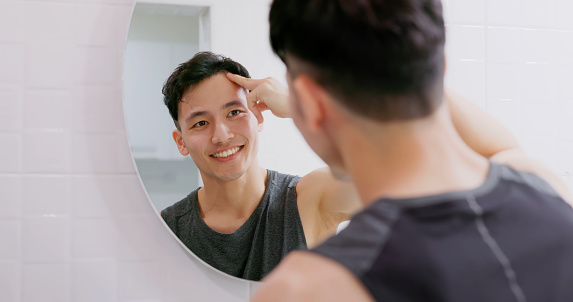 asian man use hair growing tonic in front of mirror and satisfied about the positive effect