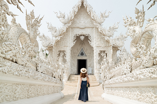A woman visiting a Buddhist temple in Chiang Mai, Thailand. She is walking towards the temple.