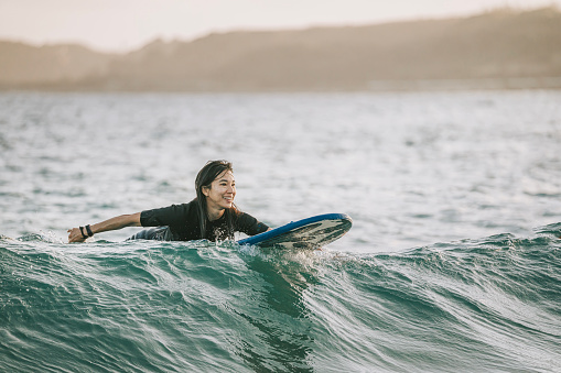Happy Asian Chinese female surfer riding wave in Taiwan Kenting beach evening
