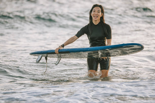 satisfied Asian Chinese female surfer returning from sea after surfing Taiwan Kenting beach evening satisfied Asian Chinese female surfer returning from sea after surfing Taiwan Kenting beach evening surfboard fin stock pictures, royalty-free photos & images