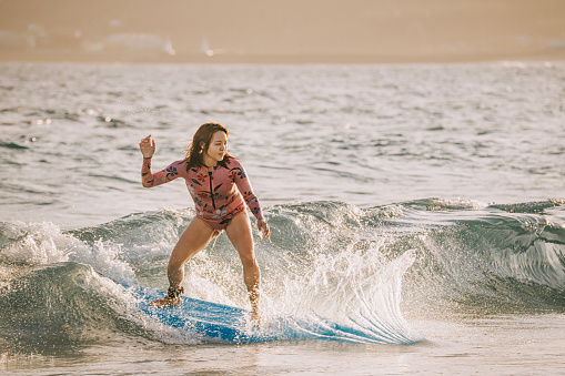 Asian Chinese female surfer riding wave surfing in Kenting beach in evening