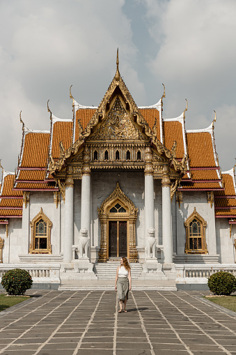 Woman posing for a photo in front of a temple in Bangkok, Thailand, she is looking to the side.