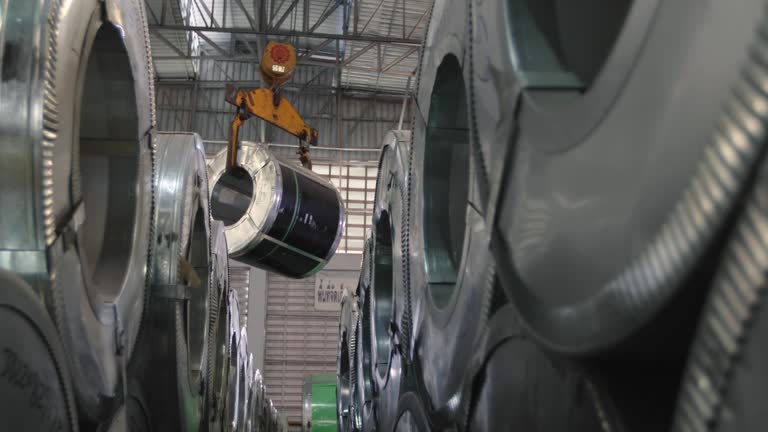 The machine is lifting the aluminum coil sheet rolled up into rolls stacked in layers on the raw material store of the manufacturing plant.