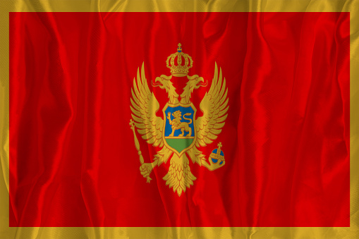 The flag of Montenegro on a silk background is a great national symbol. Texture of fabrics The official state symbol of the country