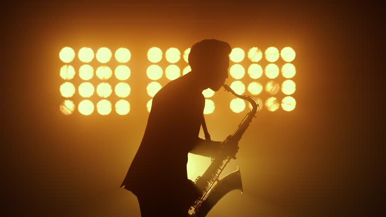 Silhouette jazz musician playing saxophone in spotlights. Man performing melody.