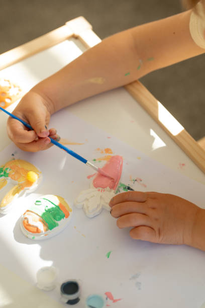 istock A cute little girl is sitting at a table and doing Easter crafts, coloring Easter figurines. Creativity and hobbies. 1473115904