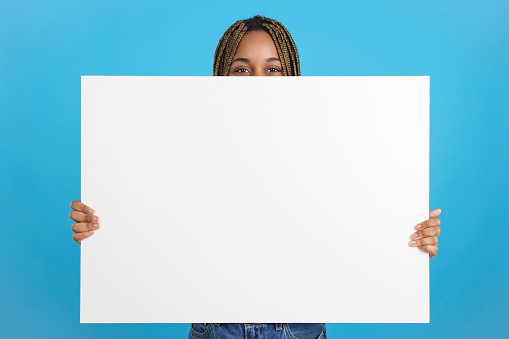 Studio portrait with blue background of an african woman holding a poster in white