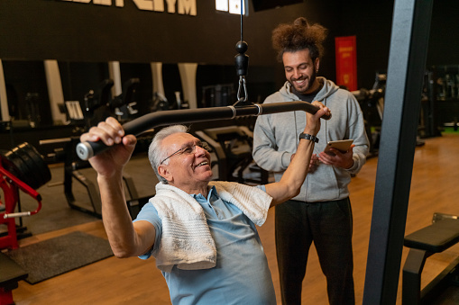 Portrait of senior man with fitness instructor pulling weight machine at the gym