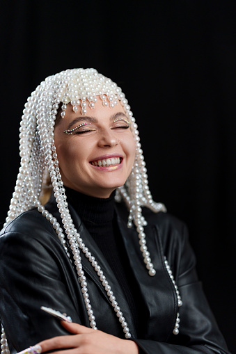 Vertical portrait of a happy woman with a wig of pearls and make up with a black background