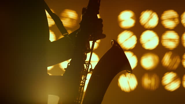 Saxophonist silhouette hands playing musical instrument in spotlights close up.
