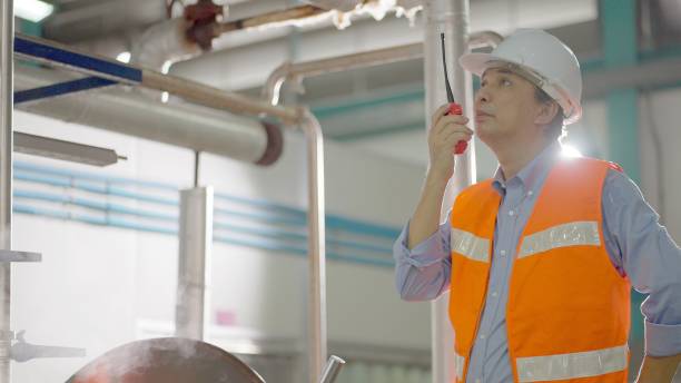 istock Asian male safety officer or manager factor or maintenance engineers or technicians or production line worker ware hard hat and safety suit, use walkie-talkie talk with team to support in repair or preparedness machine in production line at manufacturing 1473119804