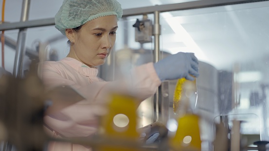 Female nutritionist or quality control officer wear sterile clothing to prevent contamination,  check production and product quality of juice filling machine in production line at manufacturing plant. Employee work in bottled fruit juice factory.