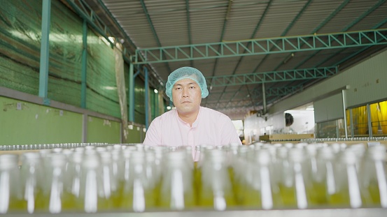 Portrait of production line worker wearing hairnet and sterile clothing, make a cart processed juices packed into bottles for pack into packaging boxes. Employee working on production line in bottled fruit juice factory. Concept of Industrial, beverage bu