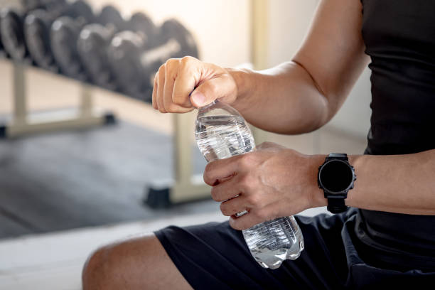 sport man with well trained body in black sportswear opening water bottle while sitting on workout bench in fitness gym. drinking water after weight training exercise. - weight training weight bench weightlifting men imagens e fotografias de stock