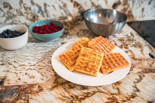 Modern kitchen countertop with waffles, fruits and kitchenware.
