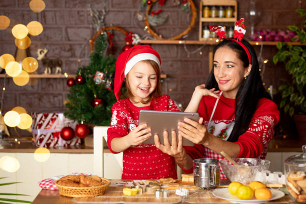 istock mom and daughter are talking via video link, passing greetings on a tablet in a dark kitchen with a Christmas tree for New Year or Christmas, smiling and having fun together in a Santa Claus hat 1473123713